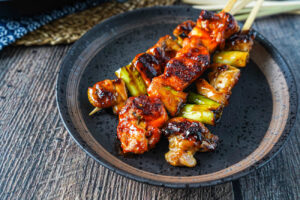 Three Dak-kkochi (Korean Sweet and Spicy Chicken Skewers) on a brown plate.