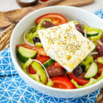Horiatiki Salata (Greek Village Salad) in a large white bowl with slices of feta on top.