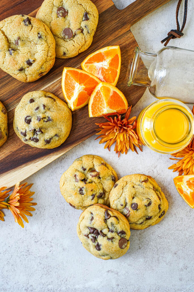 Aerial view of Orange Chocolate Chip Cookies next to orange flowers, orange slices, and orange juice.