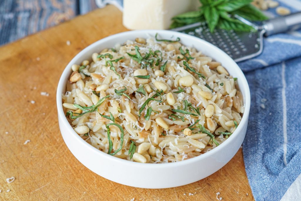 Parmesan Basil Orzo in a white bowl topped with toasted pine nuts and shredded basil.