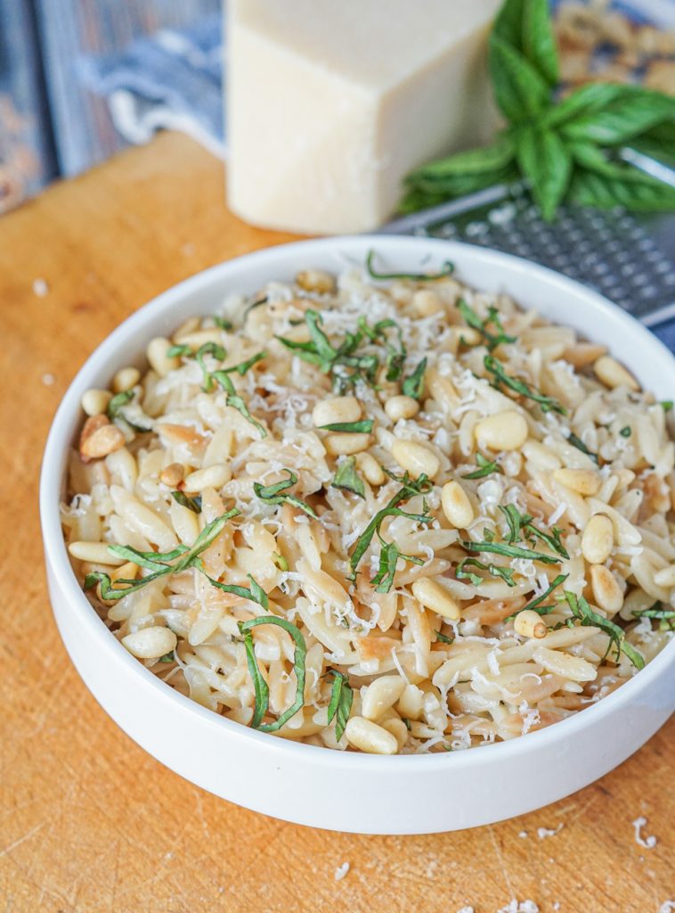 Close up of Parmesan Basil Orzo in a white bowl with pine nuts, parmesan, and basil.