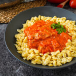 Sertéspaprikás (Hungarian Pork Paprikash) in a black bowl with pasta dumplings.