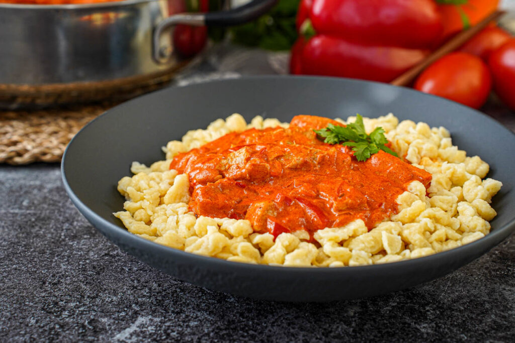 Side view of Sertéspaprikás (Hungarian Pork Paprikash) in a black bowl with pasta dumplings.