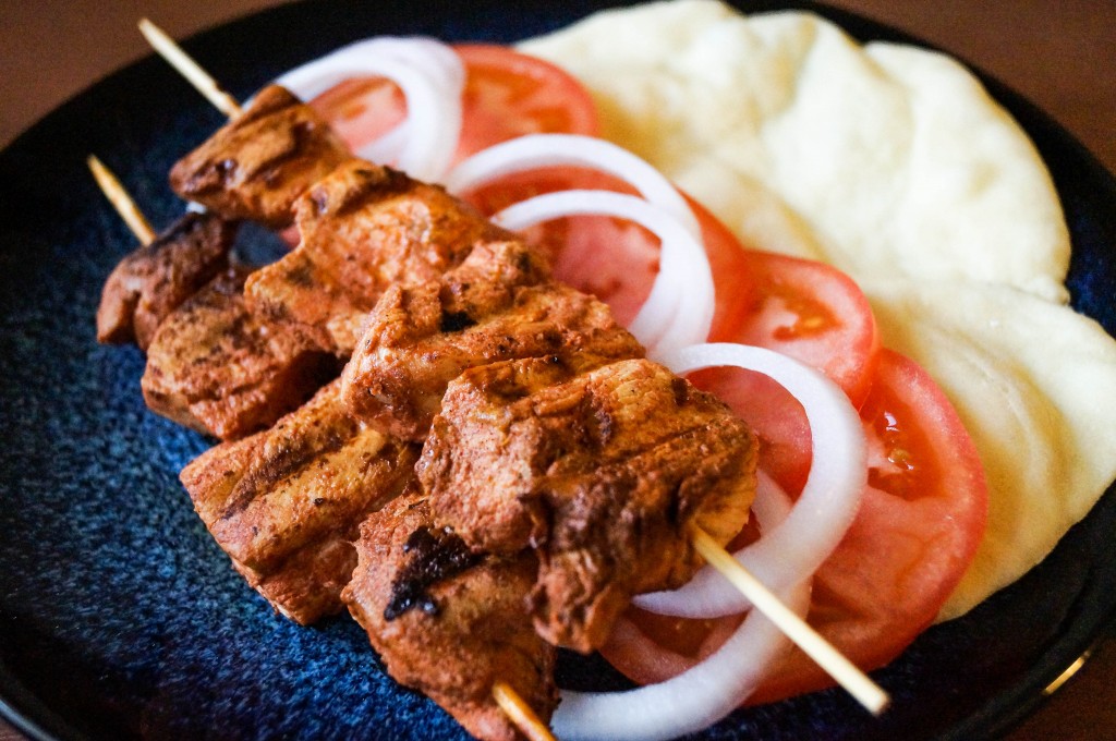 Two Shish Taouk (Syrian Chicken Skewers) on a plate with bread, tomatoes, and onions.