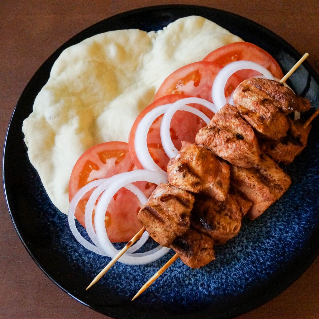 Aerial view of Shish Taouk (Syrian Chicken Skewers) on a plate with bread, tomatoes, and onions.