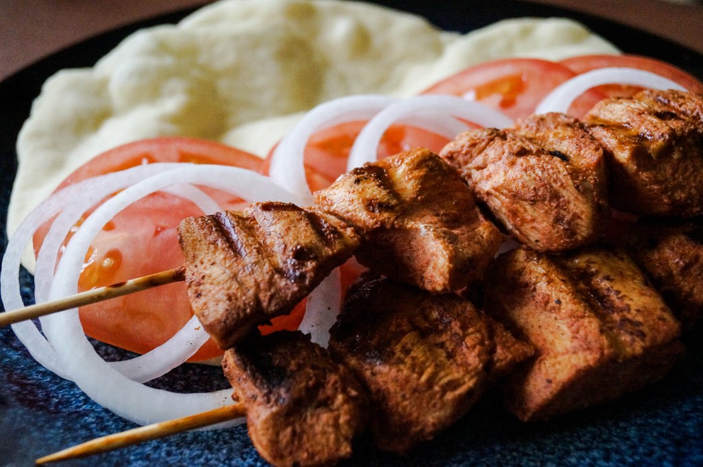 Close up of Shish Taouk (Syrian Chicken Skewers) on a plate with bread, tomatoes, and onions.