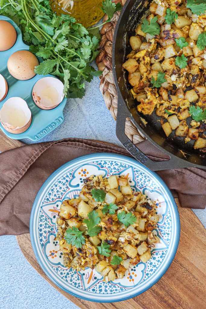Aerial view of Batata Wa Bayd (Lebanese Potatoes and Eggs) on a plate next to more in a cast iron skillet.