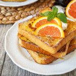 Three Slices of Orange French Toast on a white plate with orange slices.