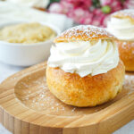 Semlor (Swedish Cream Buns) on a wooden board with almond paste in the background.