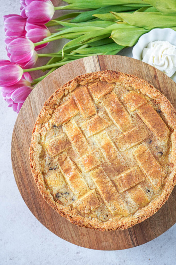 Aerial view of Chocolate Chip Ricotta Pie on a round wooden board next to pink tulips and a bowl of whipped cream.