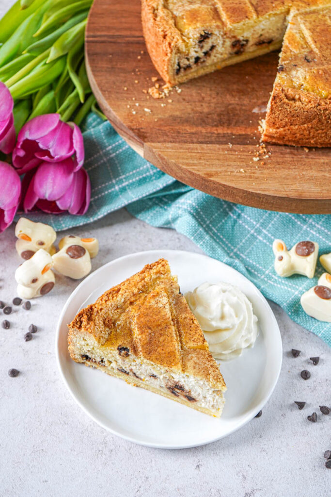 A slice of Chocolate Chip Ricotta Pie on a white plate with whipped cream and the rest of the pie on a wooden board.