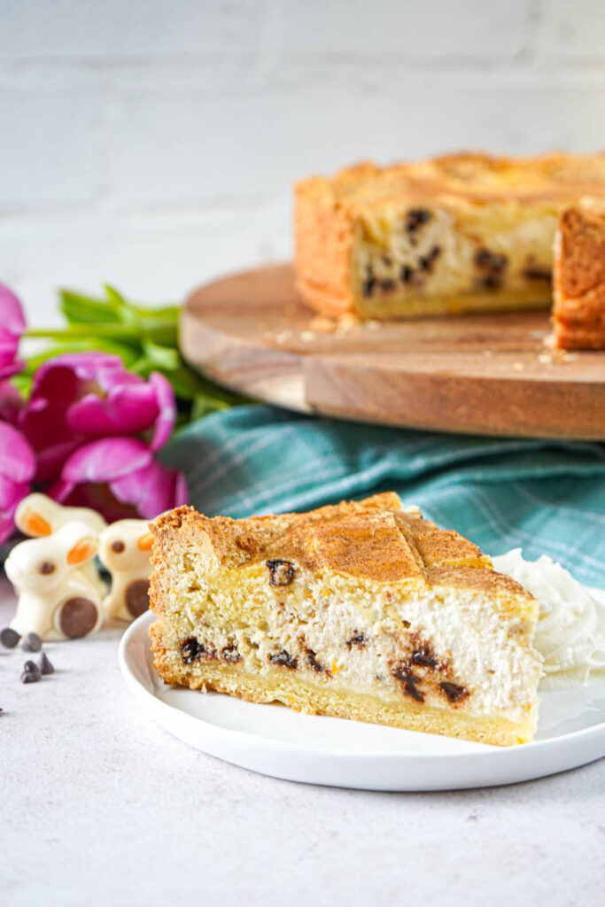 Side view of Chocolate Chip Ricotta Pie on a white plate with the rest of the pie in the background on a round wooden board.