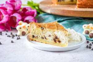 Chocolate Chip Ricotta Pie slice on a white plate with whipped cream next to chocolate chips, pink tulips, and chocolate bunnies.