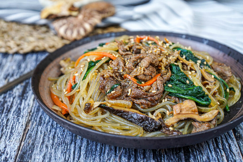 Japchae (Korean Stir-Fried Sweet Potato Noodles) in a bowl with beef, spinach, carrots, and mushrooms.