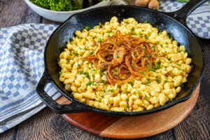 Pinzgauer Kasnocken (Pinzgau-Style Cheese Spätzle) in a cast iron skillet with fried onions.