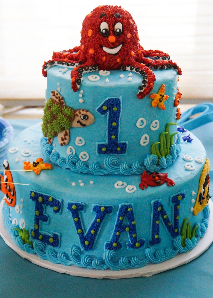 Two tier blue cake with 1, Evan, turtles, fish, and a red octopus on top.