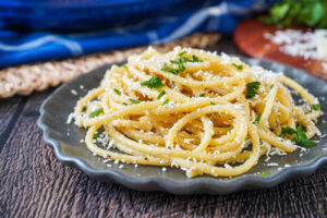 Mizithra Browned Butter Pasta on a gray plate with shredded cheese and chopped parsley.