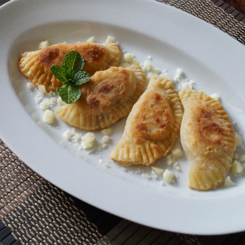 Close up of four Kremmydopitarakia Milou  (Greek Onion, Mint, and Cheese Crescents) on a white platter.