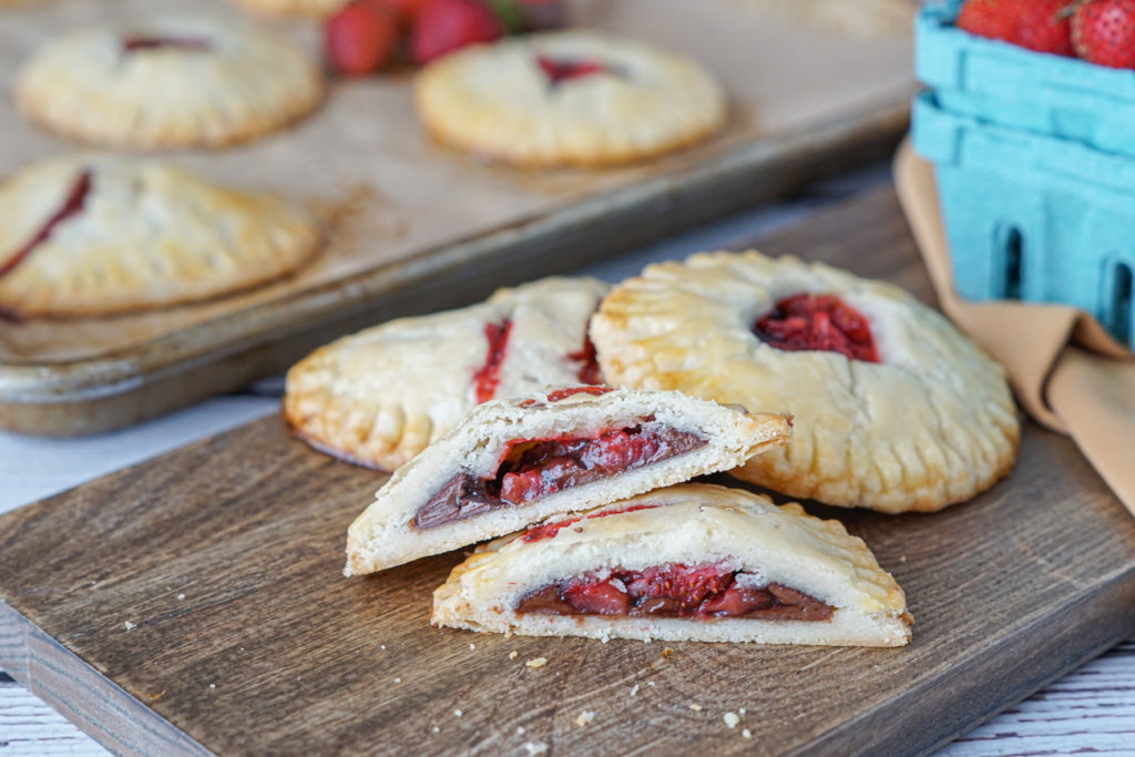 Three Strawberry Nutella Hand Pies on a wooden board with one cut in half.