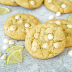 Three White Chocolate Lime Cookies next to white chocolate chips and lime slices.