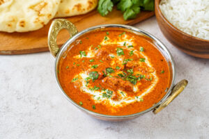 Murgh Makhani (Butter Chicken) in a bowl next to Naan, rice, and cilantro.