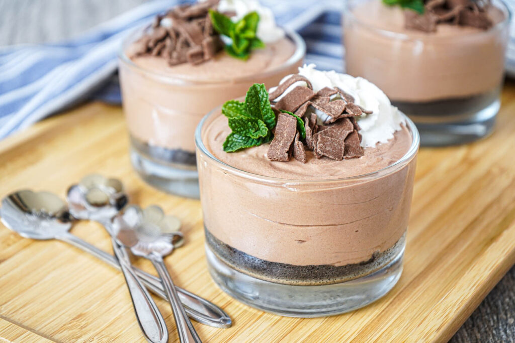 Chocolate Hazelnut Mascarpone Cups in three glasses with whipped cream, mint, and chocolate flakes.