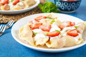 Pierogi z Truskawkami (Polish Strawberry Pierogi) on a plate with sour cream, strawberries, and mint.