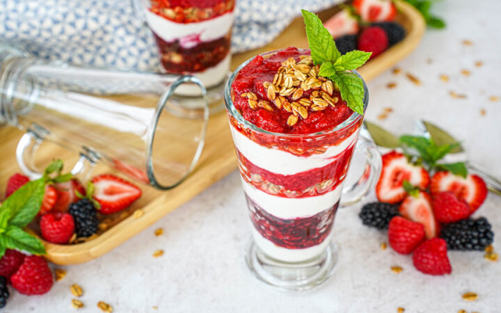Triple Berry Parfaits in two glasses next to strawberries, blackberries, raspberries, and mint sprigs.