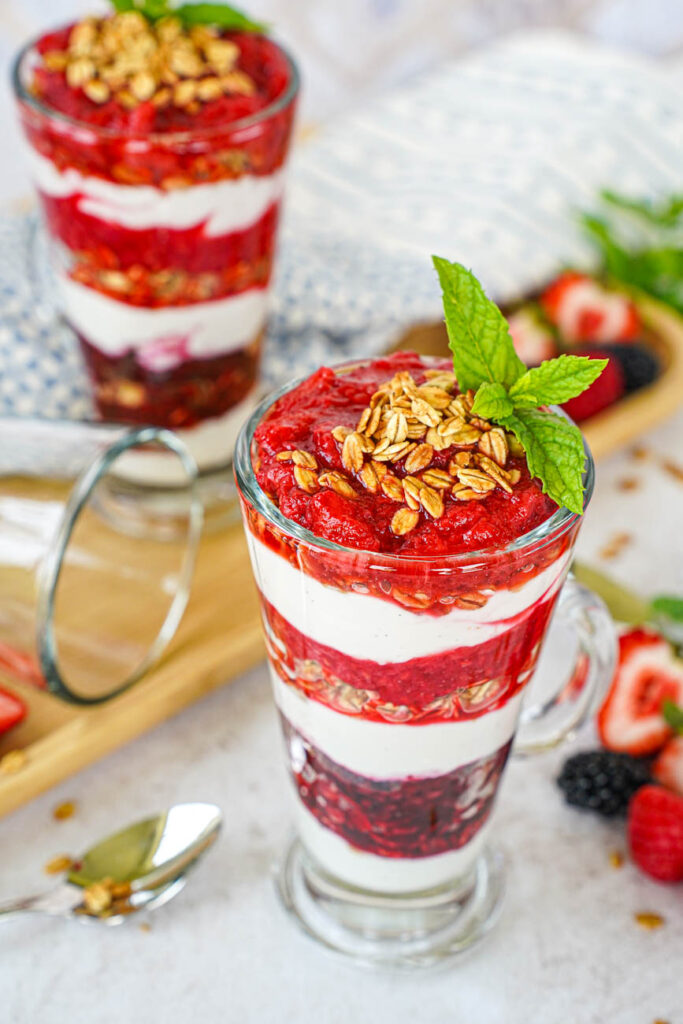 Close up of Triple Berry Parfaits in two glasses with a topping of granola and mint sprigs.