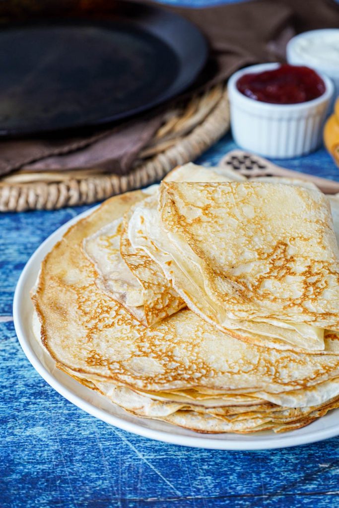 Close up of a stack of Blini (Russian Crepes) on a white plate.