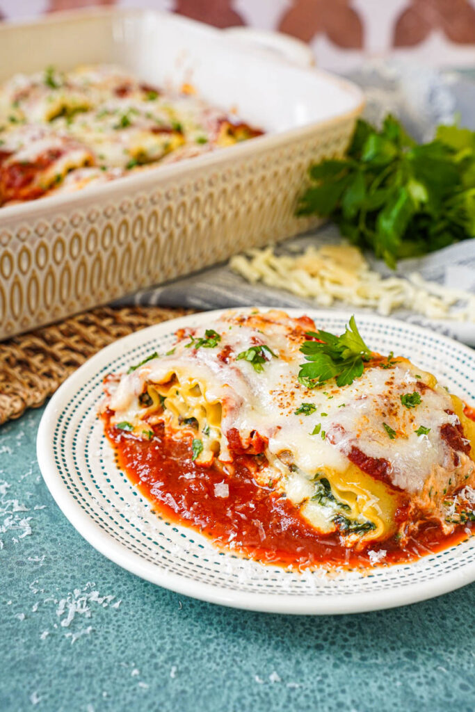 Two Mushroom Kale Lasagna Rolls on a plate with more in the background in a baking dish.