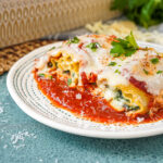 Two Mushroom Kale Lasagna Rolls on a plate with tomato sauce and fresh parsley.