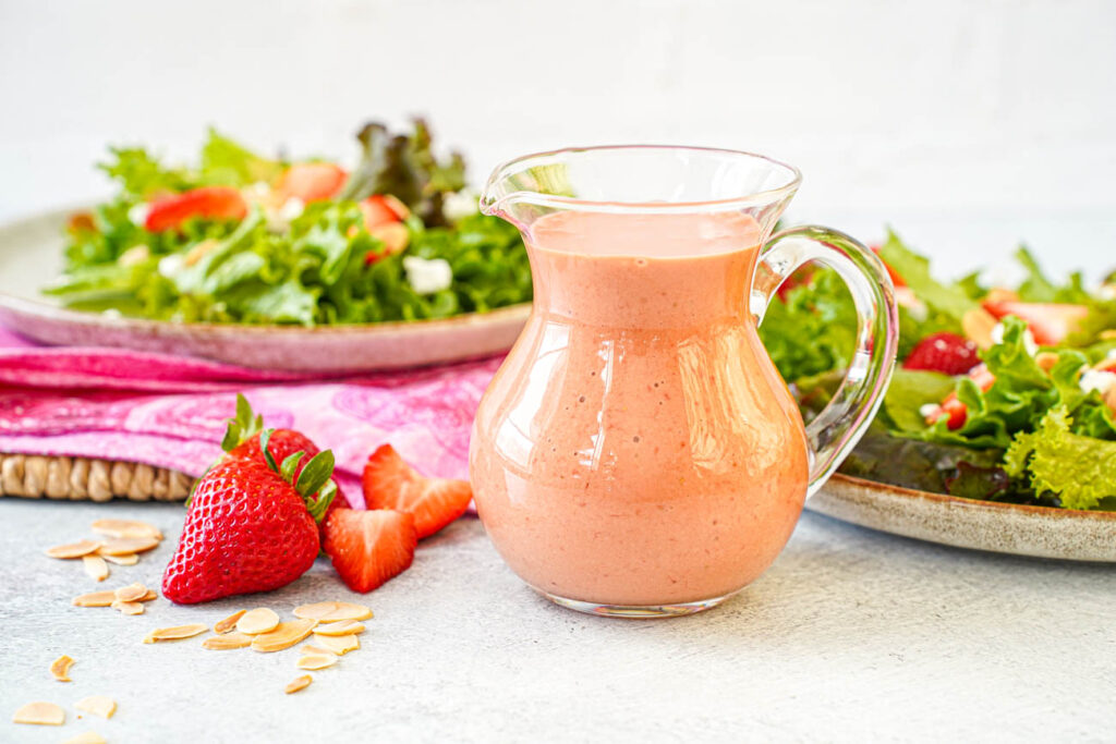Strawberry Balsamic Vinaigrette in a glass pitcher next to two plates of salads.