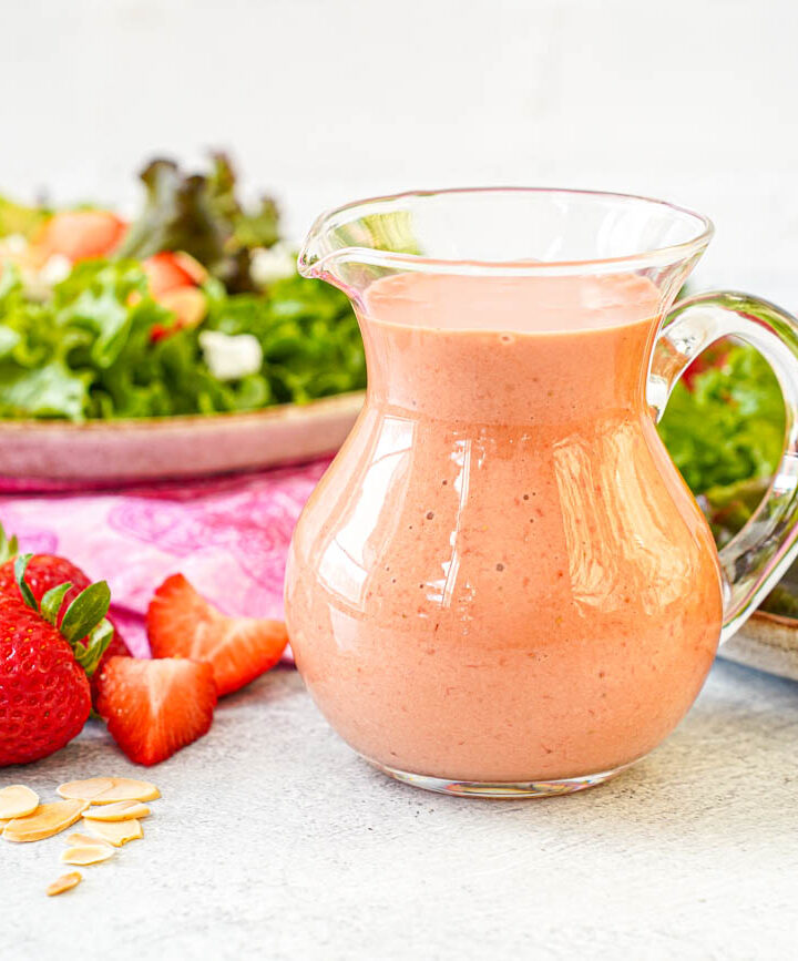 Strawberry Balsamic Vinaigrette in a glass container with two salads in the background.