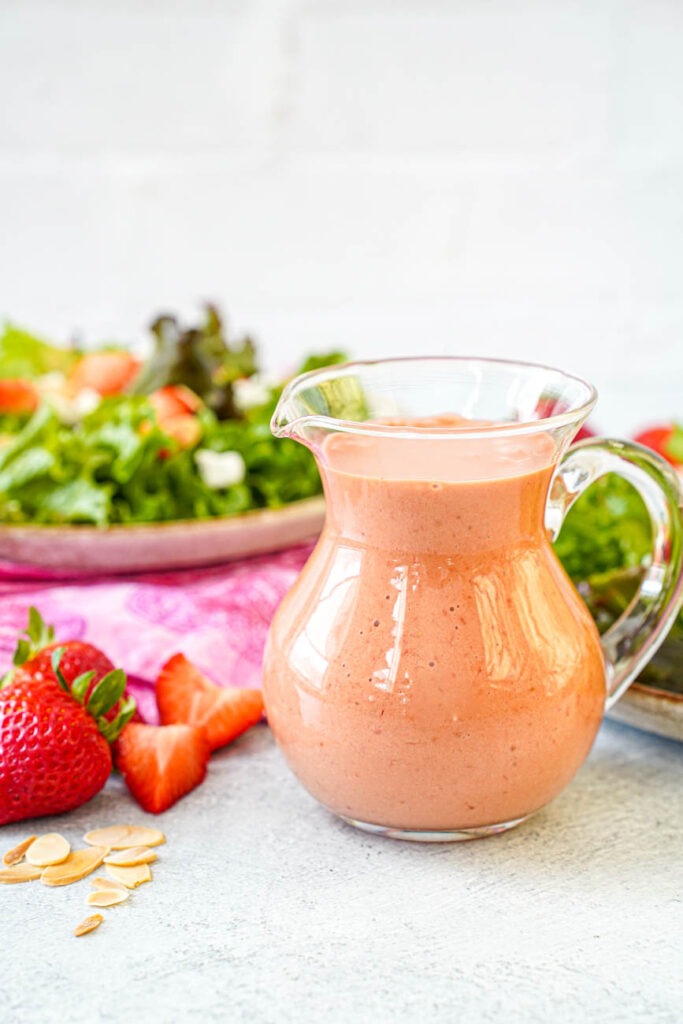 Side view of Strawberry Balsamic Vinaigrette in a glass jar with salad in the background.