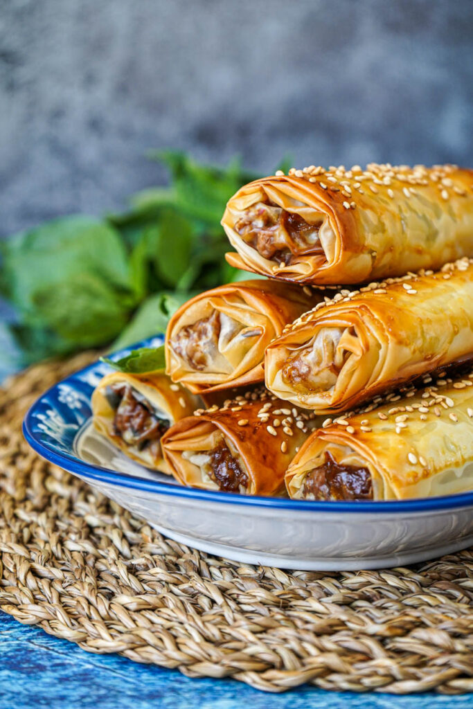 Side view of a stack of Thai Basil Chicken Phyllo Rolls with basil in the background.