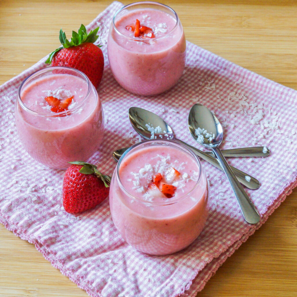 Strawberry Coconut Soup in three clear glasses next to three spoons.