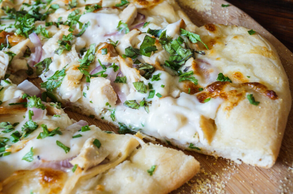 A slice of White Pizza with Chicken and Fresh Herbs on a wooden board.