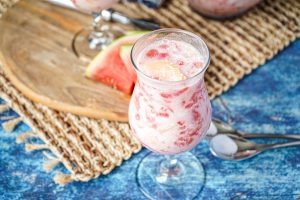 'Otai (Tongan Watermelon Drink) in a tall glass with watermelon slices in background.