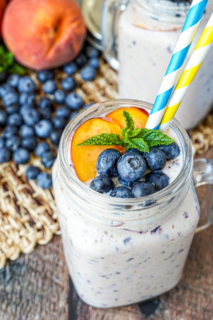 Peach Blueberry Smoothie in a handled glass mug next to scattered blueberries and peaches.