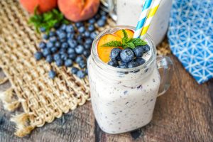 Peach Blueberry Smoothie in a handled glass with blue and yellow straws.