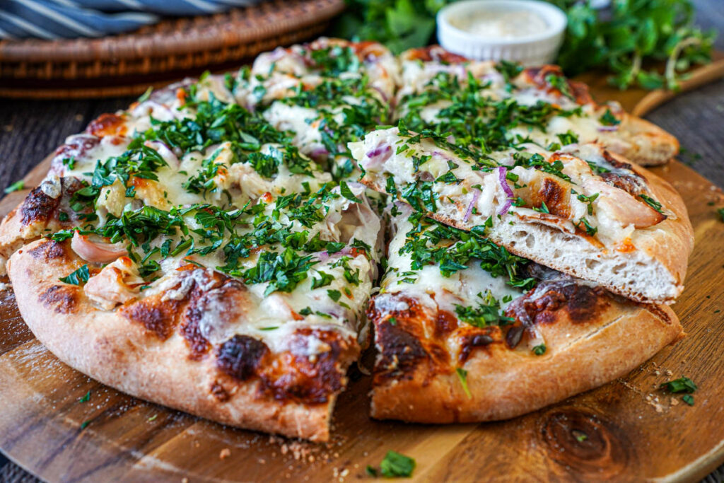 Roasted Garlic Chicken Pizza cut into slices on a wooden board.