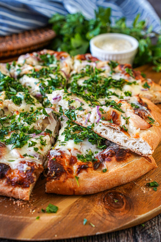 Side view of Roasted Garlic Chicken Pizza cut into slices on a wooden board.