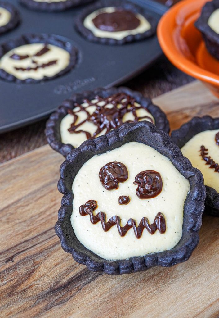 Cheesecake Tartlets with Chocolate Ganache piped into skeleton face, spider web, and jack o lanterns.