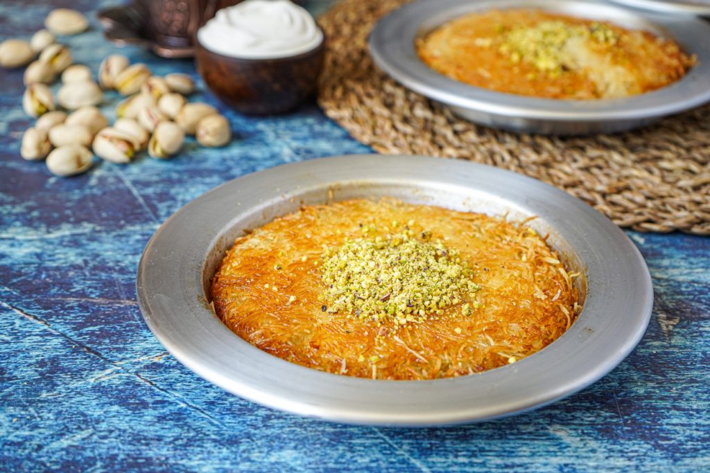 Künefe (Turkish Sweet Cheese Pastry) in two metal pans and topped with pistachios.