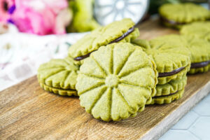A stack of flower-shaped Matcha Shortbread with Chocolate Ganache on a wooden board.