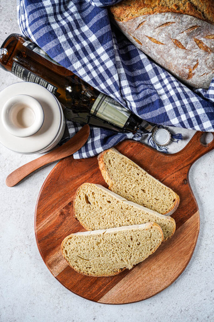 Aerial view of three slices Rustic Beer Bread on a wooden board with the loaf in the basket next to a beer bottle.