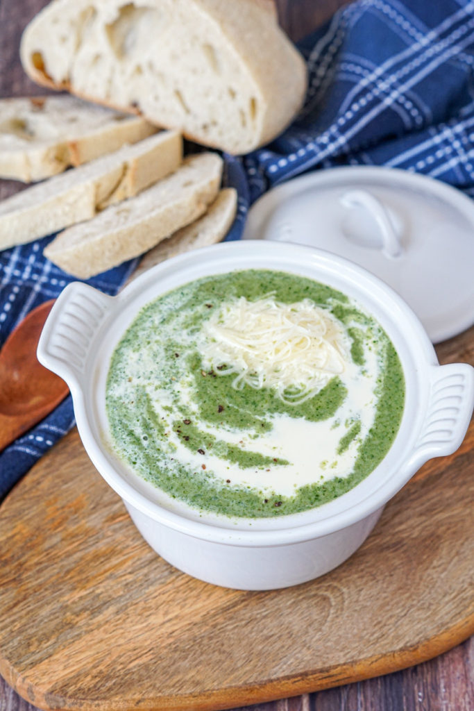 Spinach Gruyere Soup Spinach Gruyere Soup in a white soup bowl topped with cream and shredded gruyere cheese. The bowl is on a wooden board next to slices of rustic bread and a wooden spoon.