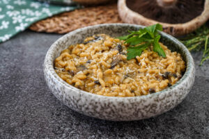 Portobello Risotto in a bowl with a spring of parsley and a portobello mushroom in the background.