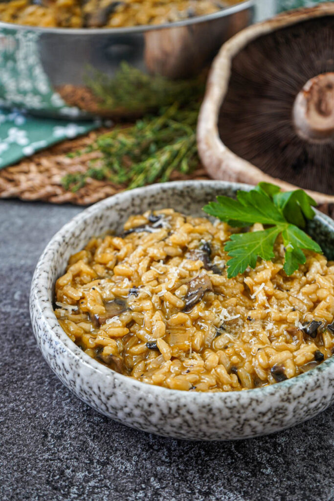 Portobello Risotto in a bowl with a pan and portobello mushroom in the background.